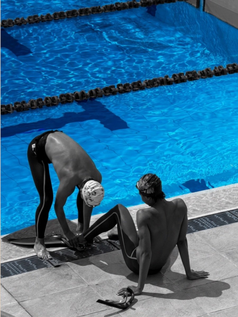 Two athletes adjusting a monofin at the pool edge