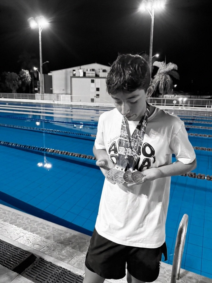 Konsta holding four competition medals by the pool at night